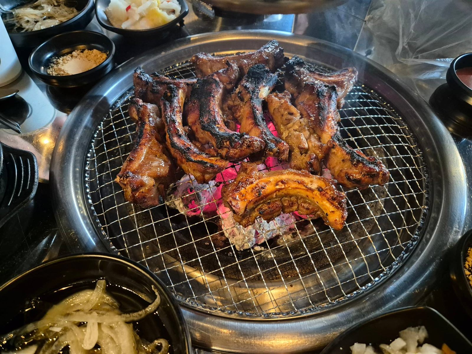록갈비 합정점 그릴 위 양념쪽갈비 — 초벌구이 후 마무리로 구워지는 모습, 주변에 반찬 그릇들이 놓여 있다